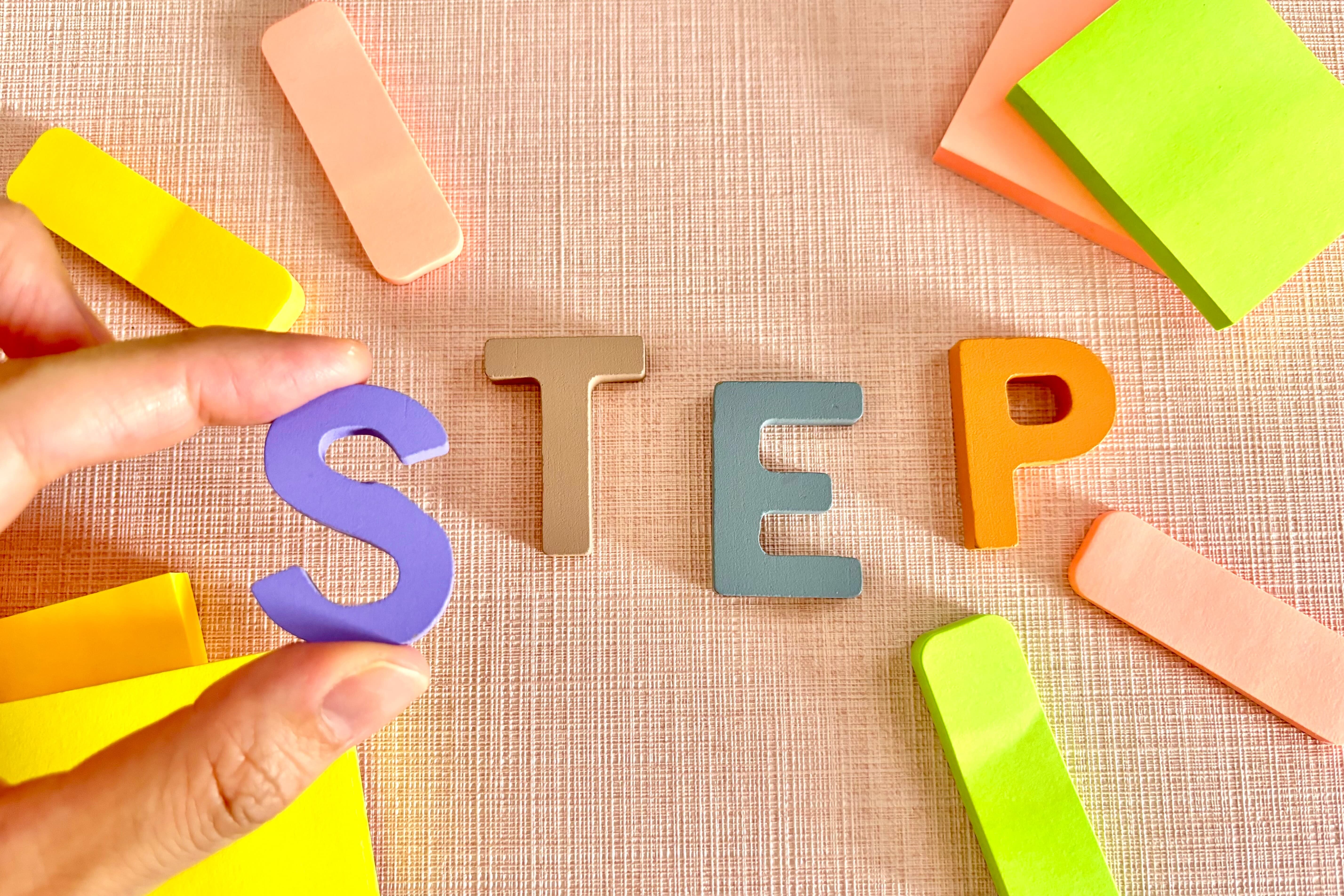 『STEP』の文字が並び、1文字を手で並べている様子。段階的な手順やプロセスを表現するイメージ。